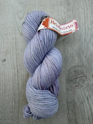 Handgefärbter Wollstrang in zartem Lilaton mit feinen rosafarbenen Sprenkeln, Garnqualität Herzfasern No 11, auf hellem Holzuntergrund.